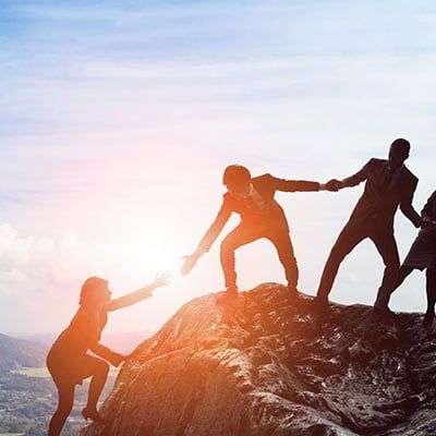 Group of coworkers helping each other climb to the peak of a mountain.